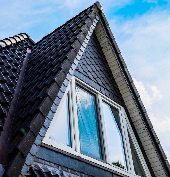 Ardoises sombres et lucarne pignon: architecture de toit élégante Lucarne pignon et toit en tuiles sombres et ardoises écailles de poisson. La fenêtre triangulaire reflète le ciel bleu éclatant.